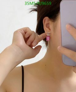 Woman showcasing pink earring with smartphone.