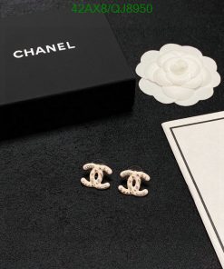 Designer earrings with brand packaging on black surface.