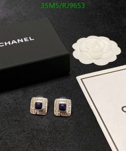 Chanel earrings, box, and logo on black surface.