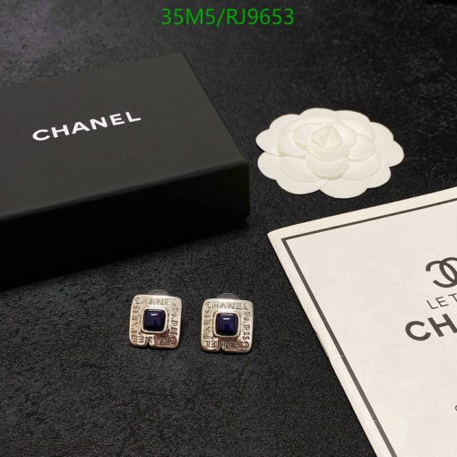 Chanel earrings, box, and logo on black surface.