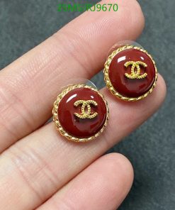 Gold-bordered, maroon earrings held between fingers.