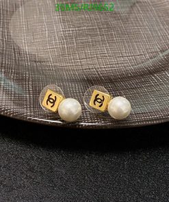 Pearl earrings with gold emblem on textured background.