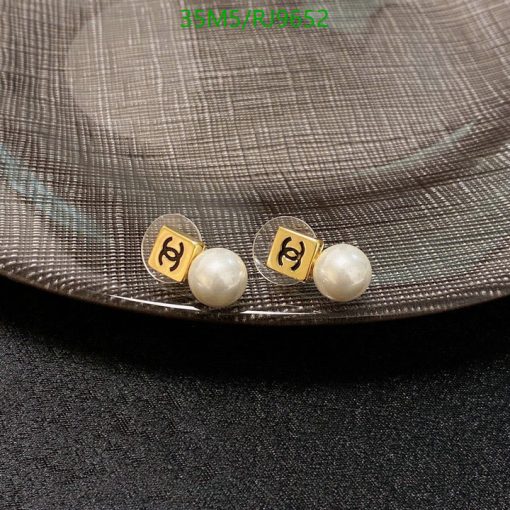 Pearl earrings with gold emblem on textured background.