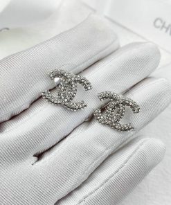 Crystal-embellished designer earrings on white gloves.