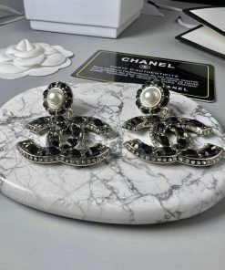 Designer pearl and logo earrings on marble surface.