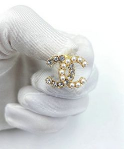 Pearl and diamond brooch held by gloved hand.