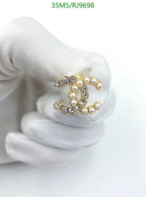 Pearl and diamond brooch held by gloved hand.