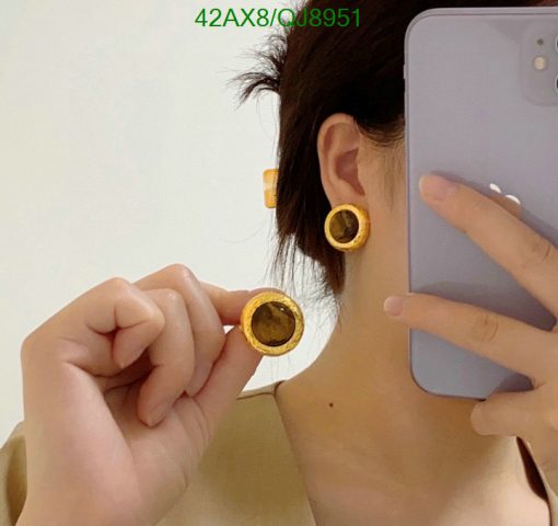 Person showcasing yellow earrings while holding a phone.