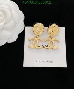 Gold designer logo earrings on white display with flower.