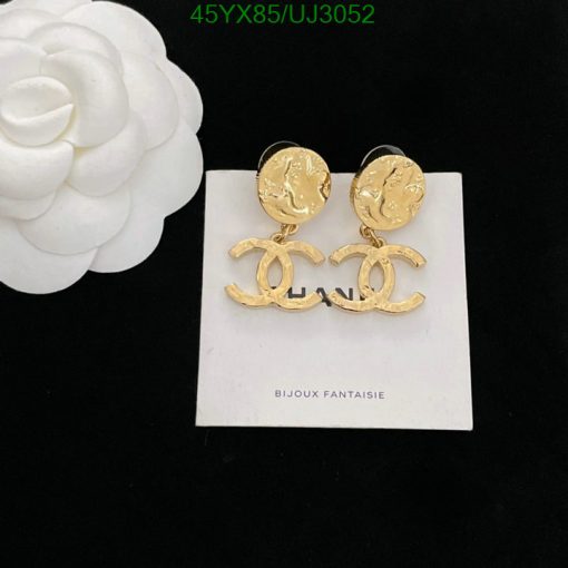 Gold designer logo earrings on white display with flower.