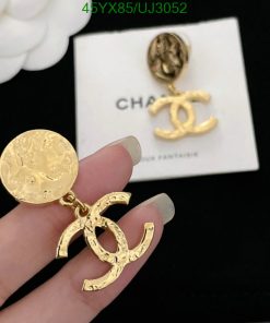 Gold designer logo earrings held by fingers.