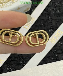 Gold designer logo earrings held by fingers.