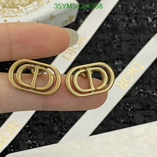 Gold designer logo earrings held by fingers.