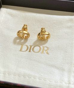 Gold designer logo earrings on branded display fabric.