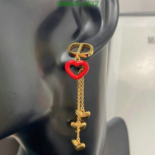 Red heart earring with gold chain on mannequin ear.