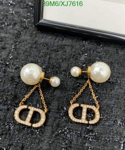 Pearl earrings with gold logo and chain on black fabric.