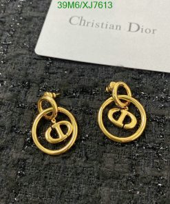 Designer gold-tone logo earrings on textured surface.