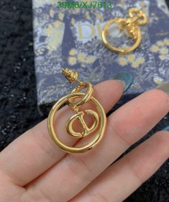 Gold designer logo earrings held over patterned card.