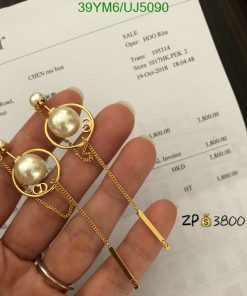 Gold pearl earrings held over an invoice.