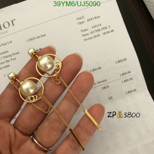 Gold pearl earrings held over an invoice.