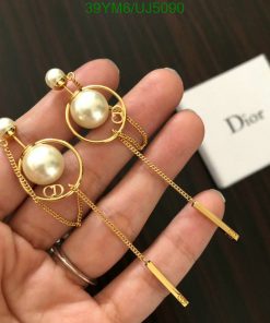 Gold pearl Dior logo earrings held over branded box.