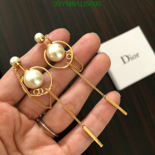 Gold pearl Dior logo earrings held over branded box.