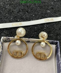 Dior pearl earrings with gold logo detail on black surface.