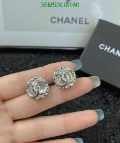 Chanel earrings held in hand with box in background.