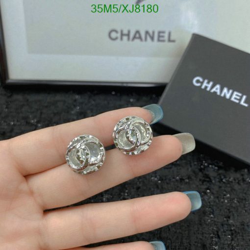 Chanel earrings held in hand with box in background.