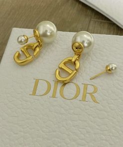 Gold Dior logo pearl earrings on white surface.