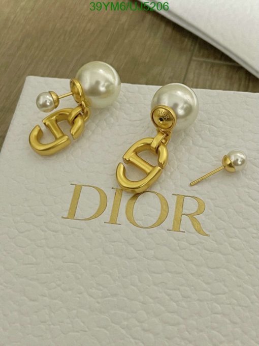 Gold Dior logo pearl earrings on white surface.