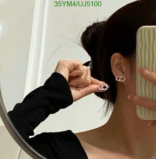 Woman trying on silver hoop earrings, mirror reflection.