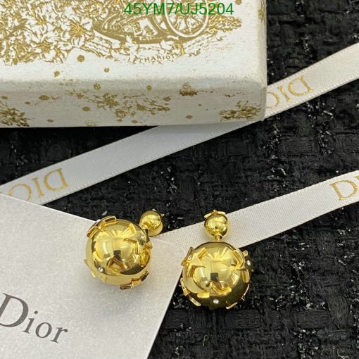 Gold Dior earrings with packaging on black texture.