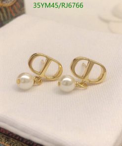 Gold pearl drop earrings on white fabric.