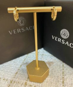 Gold earrings displayed on metal stand with designer packaging.