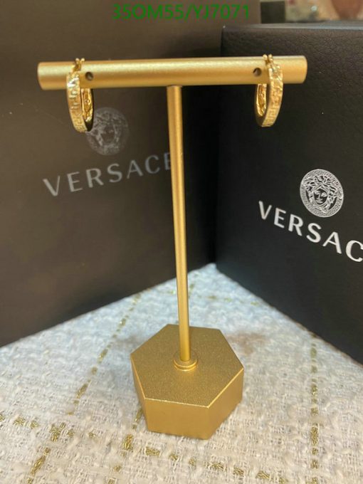 Gold earrings displayed on metal stand with designer packaging.