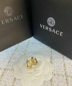 Gold Versace earrings on flower-shaped display.