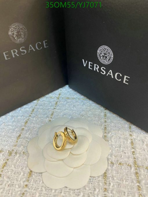 Gold Versace earrings on flower-shaped display.