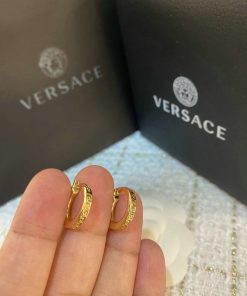 Gold hoop earrings held before branded packaging.