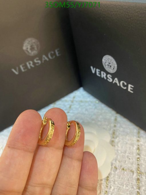 Gold hoop earrings held before branded packaging.