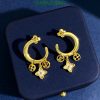 Gold charm hoop earrings on dark background.