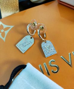 Designer hoop earrings with logo pendants on orange surface.