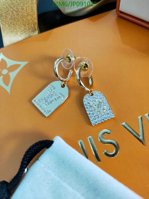 Designer hoop earrings with logo pendants on orange surface.