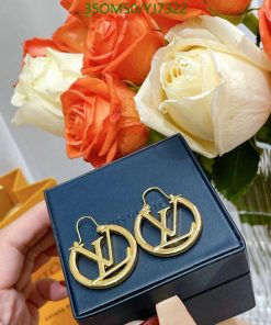 Gold designer earrings on box near orange and white roses.