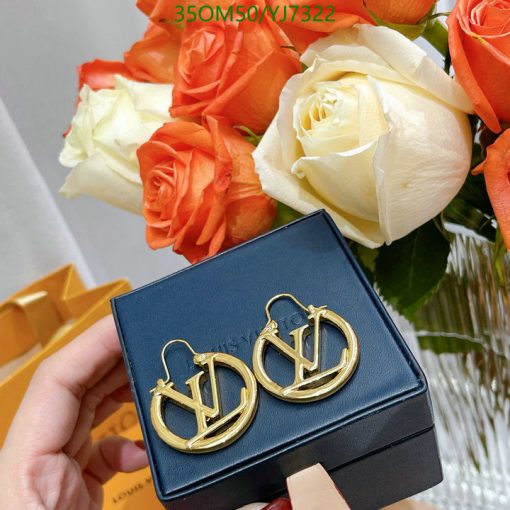 Gold designer earrings on box near orange and white roses.