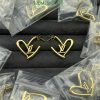 Gold designer logo earrings on black display.