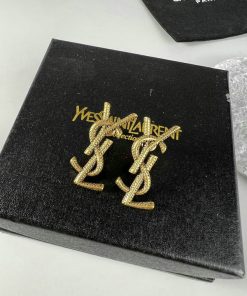 Gold designer earrings on black textured packaging.