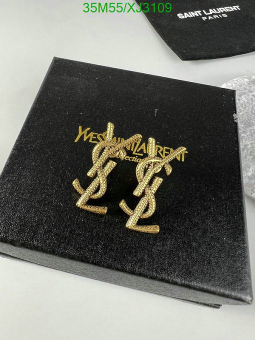 Gold designer earrings on black textured packaging.