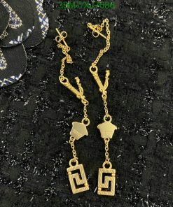 Gold designer dangle earrings on textured background.