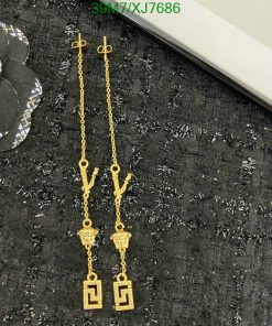 Gold dangle earrings with Greek key design on black fabric.